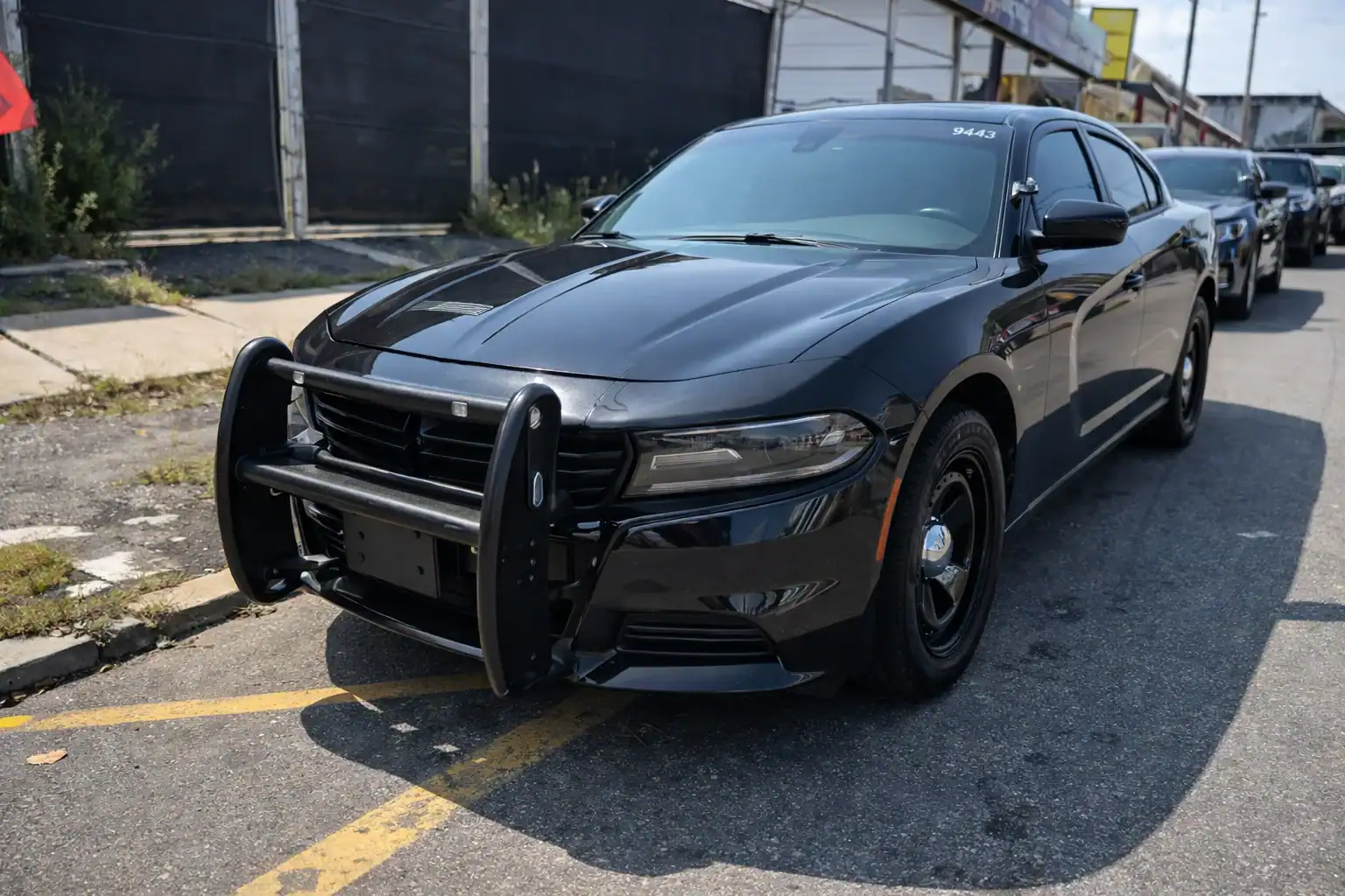 A black police interceptor NJ with a push bumper is parked on the street next to a sidewalk and buildings, commonly seen among used police cars NJ and in nearby NY and PA.