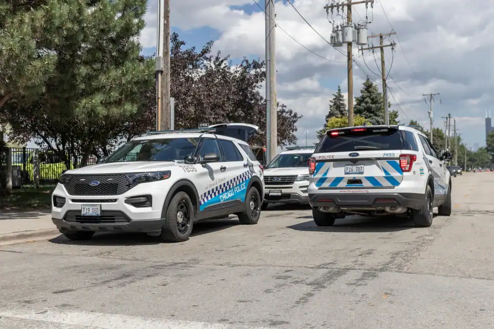 Two Chicago Police SUVs, resembling police interceptors NJ, are parked on a city street during the day. The vehicles have blue and white markings, with trees, utility poles, and a cloudy sky in the background.