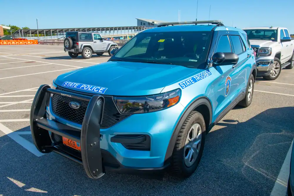 A blue Ford SUV marked as a state police vehicle is parked in a lot on a sunny day. Featuring &ldquo;STATE POLICE&rdquo; decals and a push bumper, it&rsquo;s similar to used police cars NJ, NY and PA agencies prefer. Other vehicles are visible in the background.