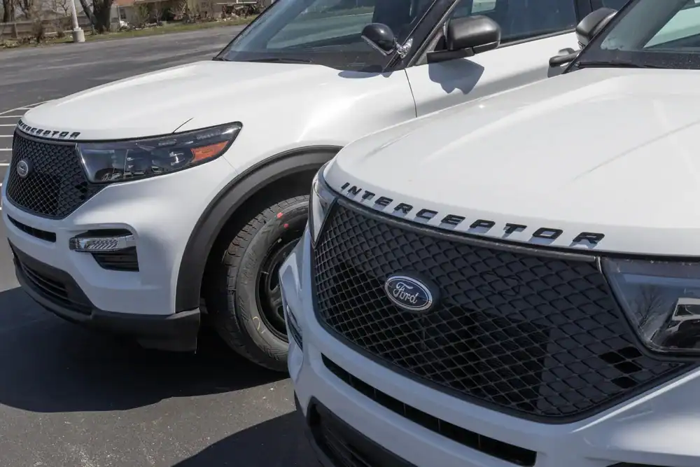 Two white Ford police Interceptor SUVs, often seen as police interceptors NJ or used police cars NJ, are parked side by side in a lot, showcasing the &ldquo;INTERCEPTOR&rdquo; marking on their hoods.